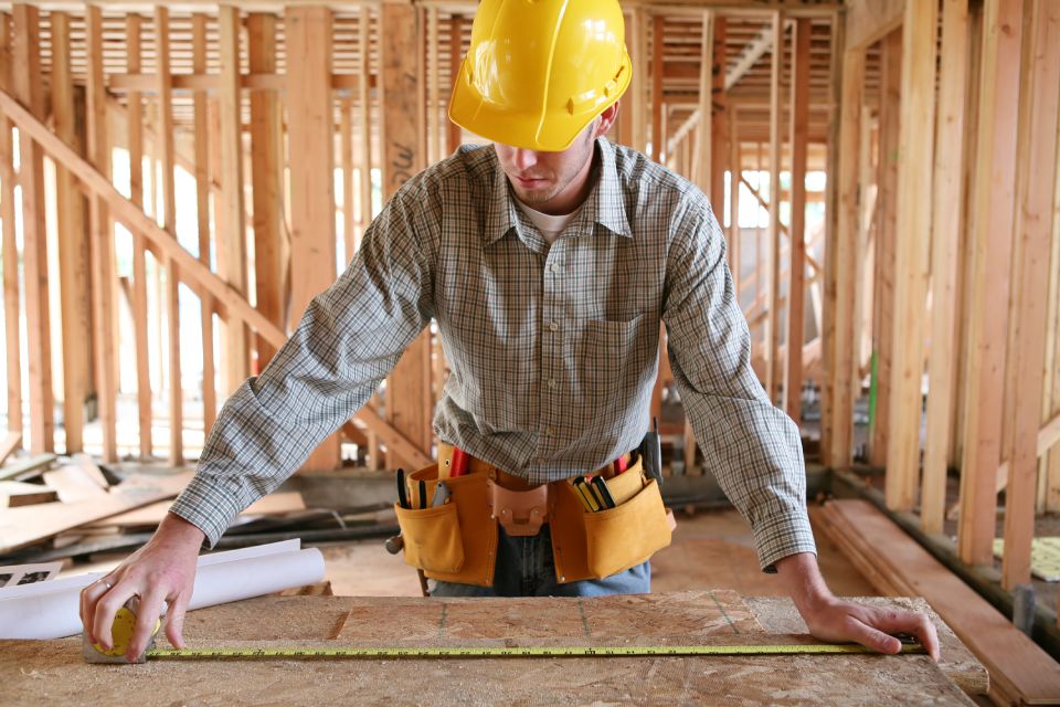 A man working building a home and measuring some wood