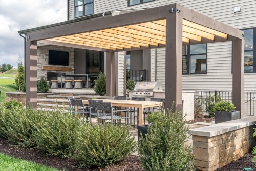 Trendy outdoor patio pergola shade structure, awning and patio roof, dining table, chairs, metal grill surrounded by landscaping