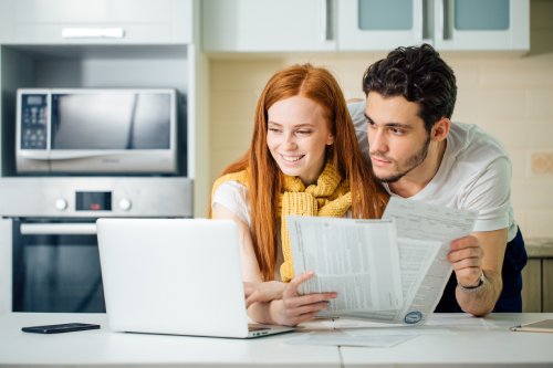 Happy couple at home paying bills with laptop and looking screen