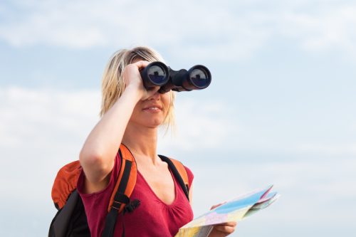 young blonde woman hiking watching through binoculars. Copy space