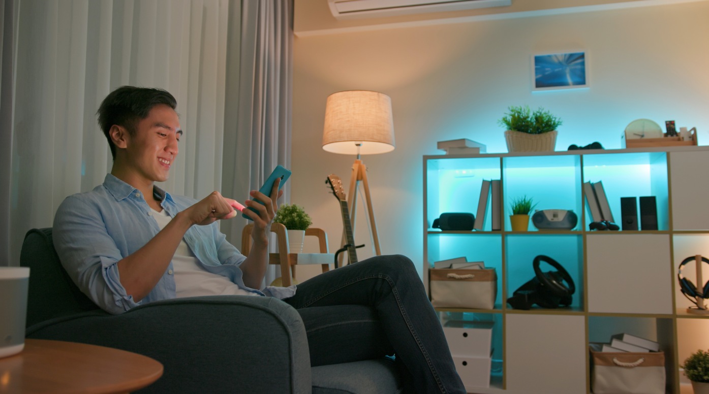 Young man using smart home app to control light colors in the evening at home