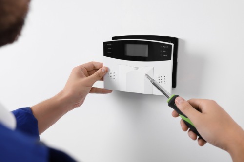 Man installing home security alarm system on white wall indoors, closeup