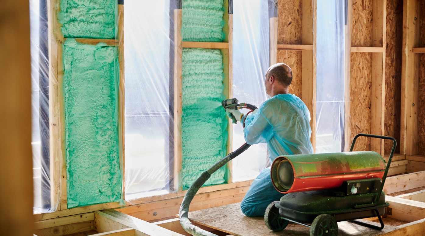 Male builder insulating wooden frame house. Man worker spraying polyurethane foam inside of future cottage, using plural component gun. Construction and insulation concept.