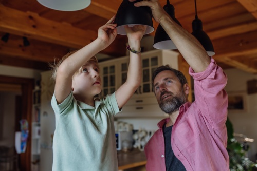 Father explaining led bubls to son, teaching him about energy efficiency, longevitiy and environmental impact. Changing bulbs at home.