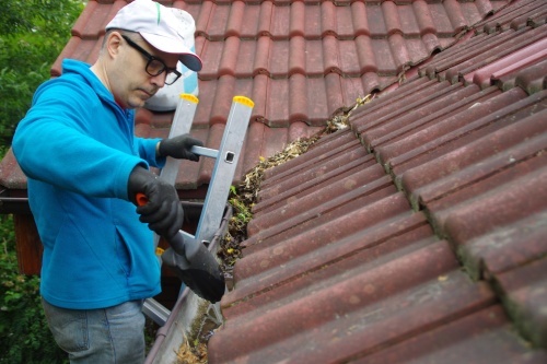 Man on ladder cleans gutter on the roof. Maintenance of a private home.