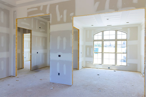 Interior view of a room with a drywall wall and a window, highlighting aspects of remodeling versus renovating.