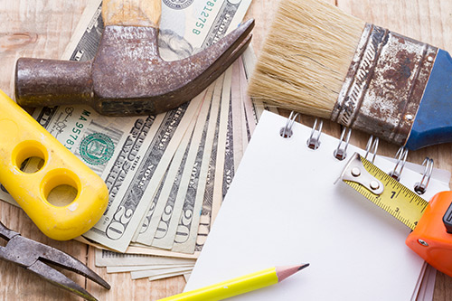 An assortment of tools alongside a stack of money on a table, highlighting a work and financial theme.