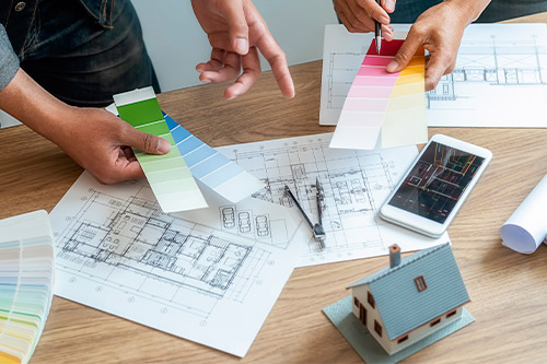 Two people are engaged in a home design project, analyzing blueprints and sharing ideas at a workspace.