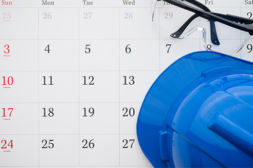 On a desk, a hard hat, protective glasses, and a calendar are displayed, suggesting preparation for a construction project.