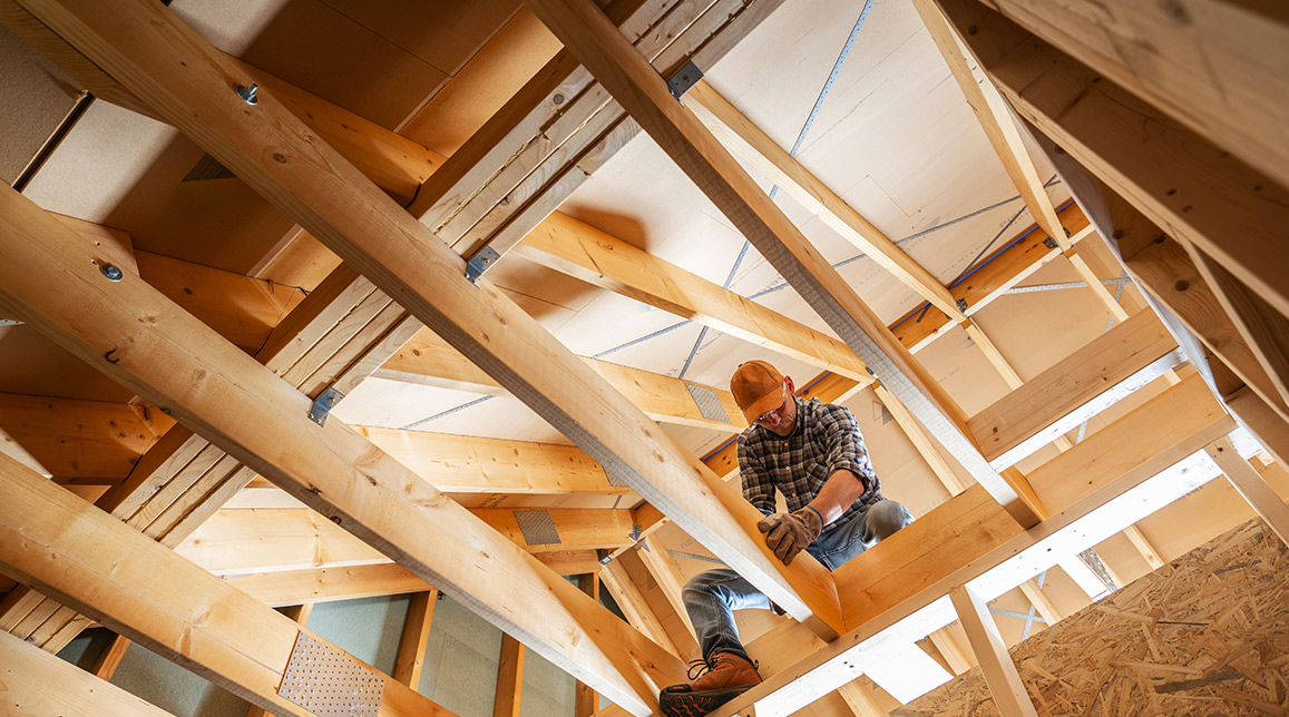 A man works on a house roof, focused on construction during winter, highlighting home-building challenges in cold weather.