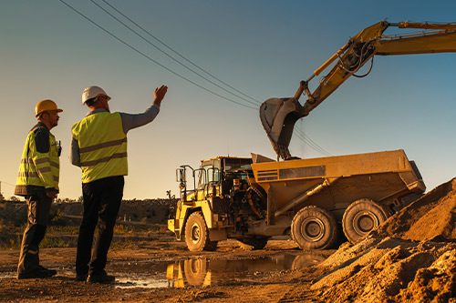 Two men wearing yellow vests are next to a dump truck, illustrating the impact of construction on McAllen's economic development.