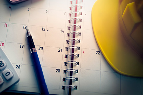 A calendar with a hard hat, calculator, and pen, representing planning for home construction ahead of hurricane season.
