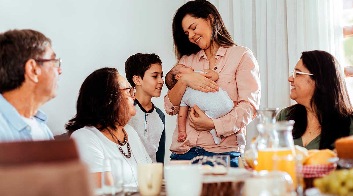 Happy Brazilian multi-generation family having breakfast together and talking at the table. Extended family meeting the newborn.