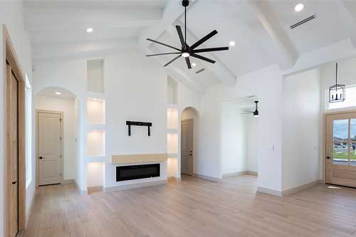 An expansive, vacant room with plain white walls and a ceiling fan, emphasizing simplicity and openness.