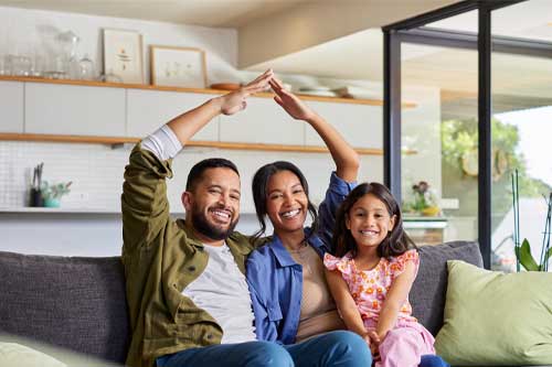  Four family members on a couch, joyfully raising their arms in a cheerful pose.